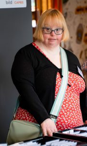 A photo of Kate Brackley. She is a woman with short blonde hair and glasses wearing a red dress.