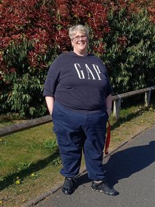 A photo of Sal. She is a woman with cropped grey hair. She is wearing a GAP shirt, glasses and smiling